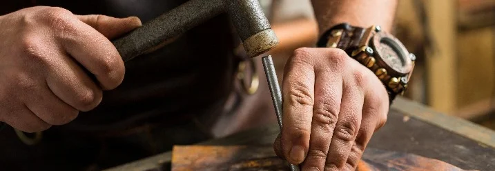 Person bearbeitet Metall mit Hammer und Meißel
